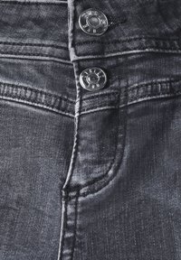 Jeans en denim gris foncé avec un léger éclat. Présente deux boutons en métal, des coutures apparentes et une poche avant avec un bord arrondi.