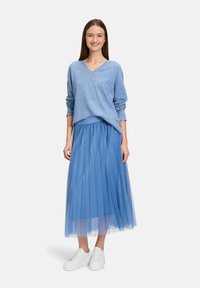 Übergröße blauer Pullover aus weichem Strick, mit V-Ausschnitt. Fließender, plissierter blauer Tüllrock. Weiße Sneakers runden das Outfit ab.