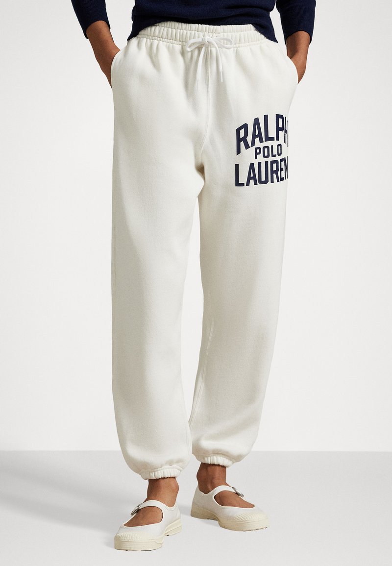 White sweatpants with a drawstring waist, featuring a large navy blue "RALPH LAUREN" logo. Cuffed hems and soft, textured fabric.