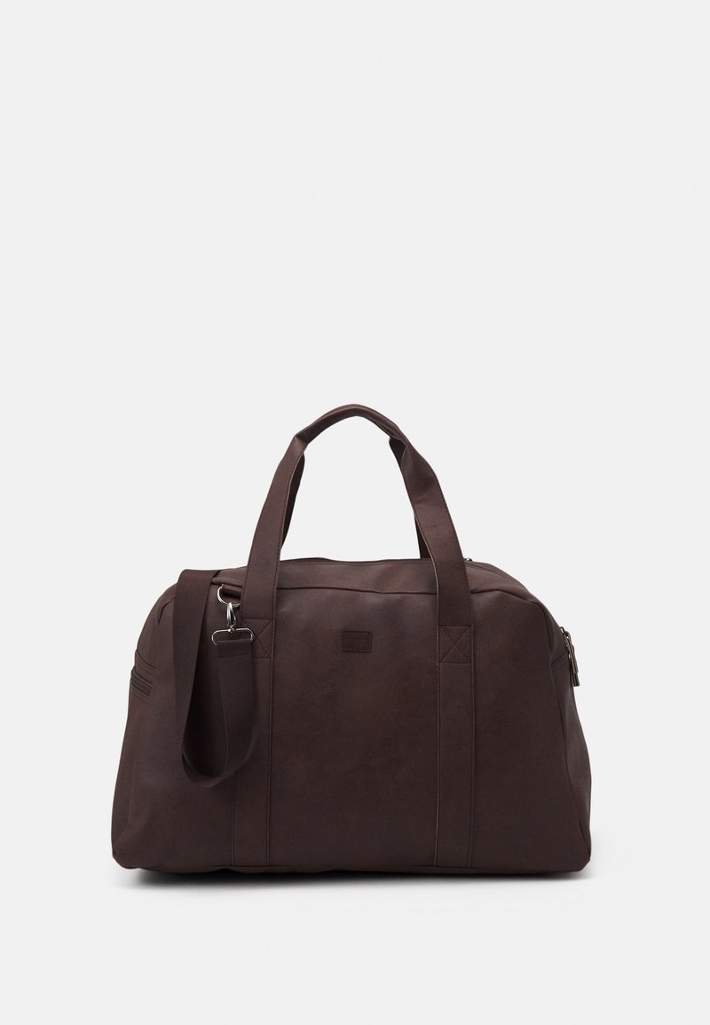 Sac polochon en cuir marron foncé avec deux poignées et une bandoulière amovible sur un fond blanc uni.