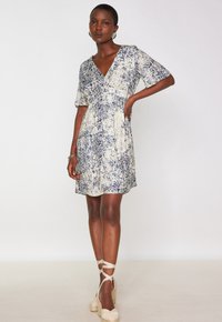 Abito a maniche corte, scollatura a V profonda in crema con motivo floreale blu, tessuto morbido, vita aderente e gonna fluente, abbinato a leggeri espadrillas.