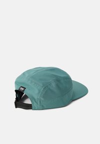 Teal cap with a curved brim, made of textured fabric. Features a rear adjustable strap and a small logo tag on the side.