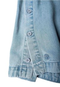 Svjetloplavi rub denim jakne s tri gumba, rupicama za gumbe, dvostrukim šivanjem i malim vezenim okruglim logotipom blizu donjeg ruba.