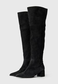 Botas de ante negras sobre la rodilla con puntera afilada, tacón cuadrado y una textura suave con costuras a lo largo del cañón.