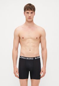 Schwarze Boxershorts mit einem weißen Bund, auf dem der Text "BJÖRN BORG" steht. Glattes Material, enganliegendes Design und eine Länge bis zur Mitte des Oberschenkels.