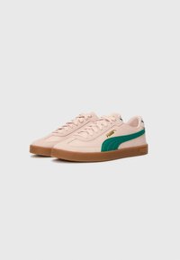 Svijetlo ružičaste patike s zelenim detaljima, teksturirana nubuk gornja strana, gumeni potplat boje karamele i bijele vezice. PUMA logo u zlatnoj boji. Klasičan dizajn.