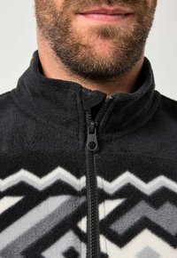 Chaqueta de forro polar negra con un alto cuello, que presenta un patrón geométrico en gris y blanco. Tiene un cierre frontal con cremallera y una textura suave.