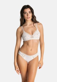 Ensemble de lingerie en dentelle beige doux, comprenant un triangle bralette avec bretelles réglables et un bas de culotte taille basse assorti, mettant en valeur de délicats motifs floraux.