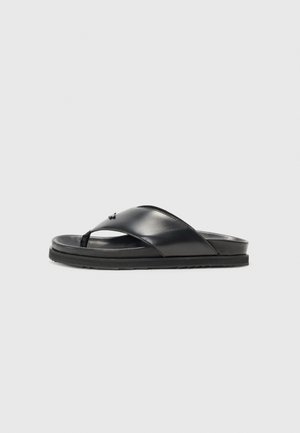 Black leather flip-flop sandals with a flat sole, featuring a wide strap across the foot and a small branded accent on the top.