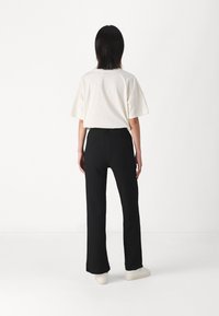 T-shirt en coton crème à coupe décontractée associé à un pantalon large à taille haute noir texturé et des baskets blanches, vu de l'arrière.