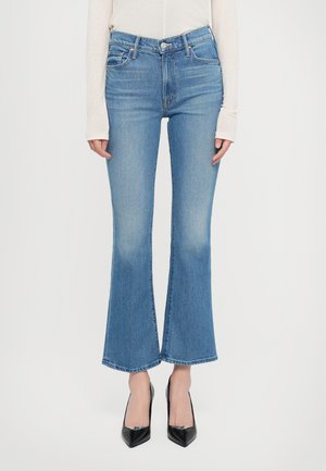 Flared blue denim jeans with a high waist, subtle fading, and a raw hem, paired with black pointed heels. Smooth texture.