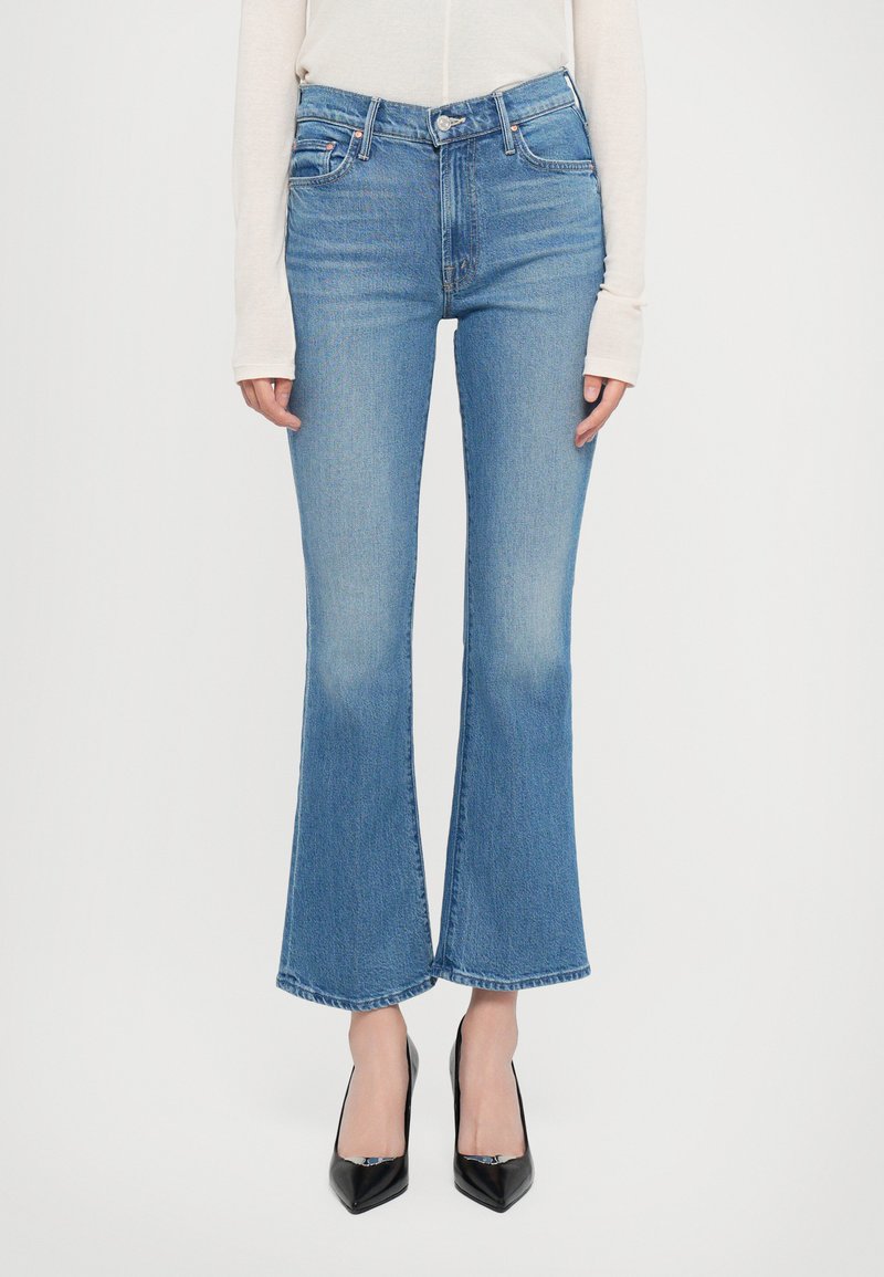 Flair blauwe denim jeans met een hoge taille, subtiele vervaging en een rafelige zoom, gecombineerd met zwarte puntige hakken. Glad textuur.