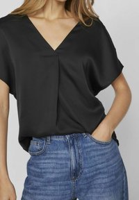 Top in satin nero con scollatura a V, vestibilità rilassata e maniche corte. Abbinato a jeans in denim azzurro chiaro a vita alta. Texture liscia.