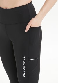 Zwarte sportleggings met een hoge tailleband, zijzak en wit merklXogo. Soepele textuur met een aansluitend ontwerp en subtiele accentdetails.
