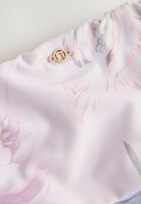 Blommönstrad tyg i pastellnyanser av rosa och blått, med en texturerad yta och en dekorativ detalj i guldton.