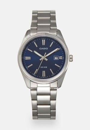 Silver stainless steel wristwatch with a navy blue dial, metallic hour markers, and a date window at 3 o'clock. Water-resistant to 50 meters.
