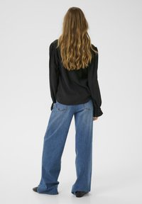 Black long-sleeve top and high-waisted wide-leg blue jeans, presenting a relaxed fit. The material appears soft with visible stitching details.