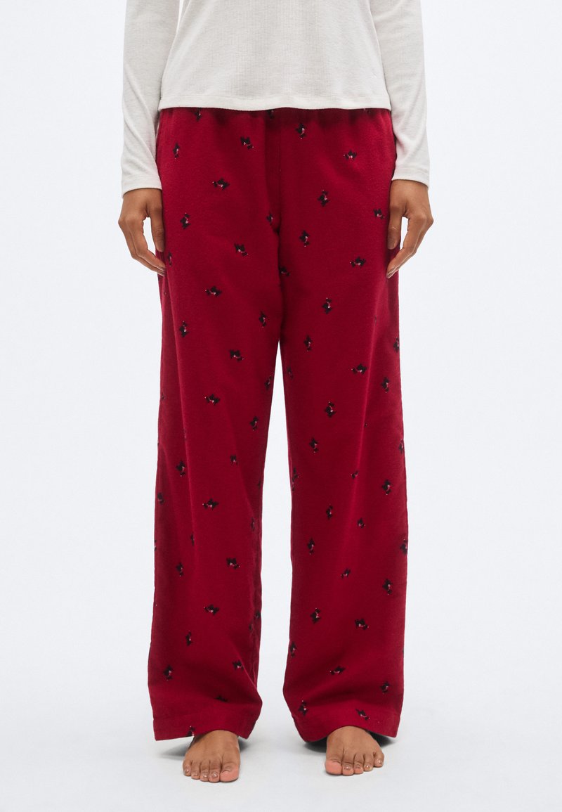 Pantalon de pyjama en molleton rouge avec des accents de motifs noirs, présentant une coupe décontractée et une taille élastique. Le tissu semble doux et confortable.