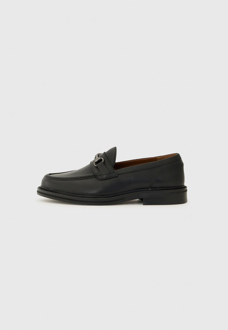 Schwarze Leder-Einlaufschuhe mit runder Zehenform, dekorativem Riemen mit silberner Hardware und einer niedrigen, strukturierten Sohle. Klassisches Design mit minimalen Akzenten.