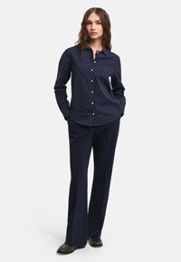 Navy blue button-up shirt with white polka dots, long sleeves, and a collar, paired with dark trousers and brown shoes.