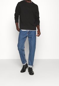Schwarzer Langarm-Sweatshirt kombiniert mit hellblauen Denim-Jeans, ergänzt durch hochgekrempelte Ärmel und schwarze Stiefeletten. Einfacher, lässiger Look.