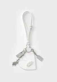 Porte-clés en cuir blanc en forme de cœur avec une chaîne en argent, présentant des accessoires étincelants et des étiquettes. Texture lisse avec une finition brillante.