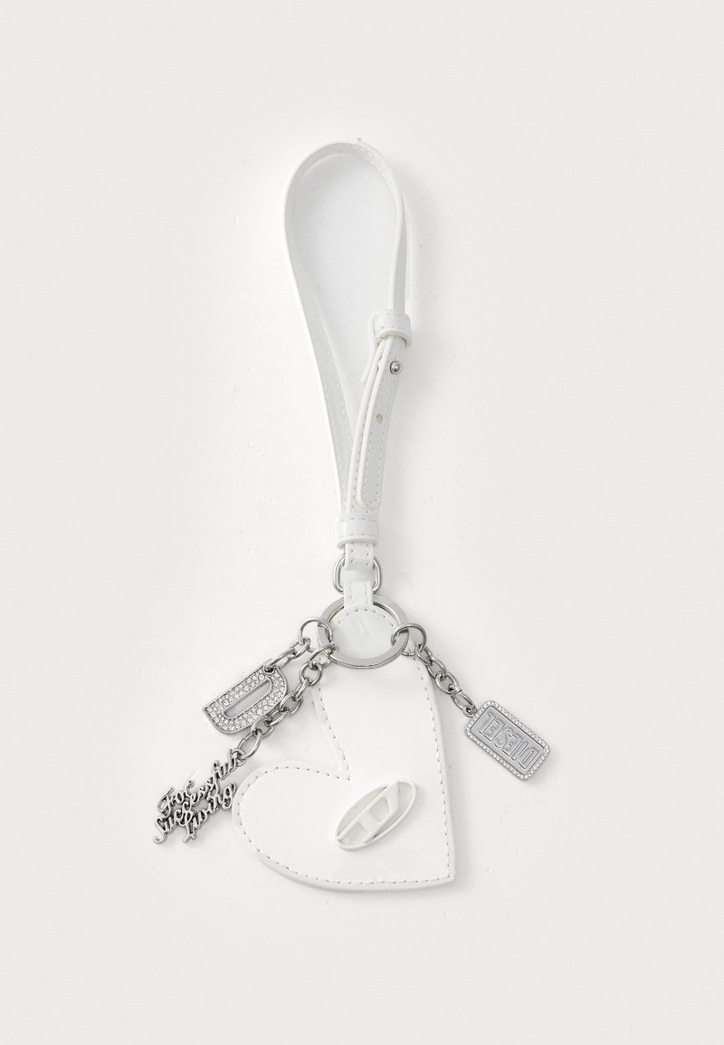 Porte-clés en cuir blanc en forme de cœur avec une chaîne en argent, présentant des accessoires étincelants et des étiquettes. Texture lisse avec une finition brillante.