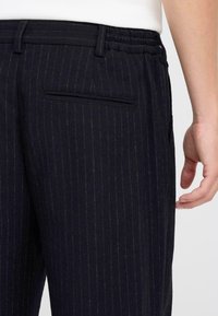 Marineblauwe pinstriped broeken van zachte stof, met een elastische tailleband en een achterzak met een smalle slitopening.