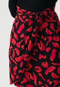 Gonna nera avvolgente con un motivo astratto di forme rosse e arancioni. Realizzata in tessuto morbido ed elastico con un dettaglio di cintura annodata.