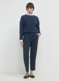 Navy gestrickter Pullover mit Rippstruktur, kombiniert mit navy blauen maßgeschneiderten Hosen. Das Outfit wird durch schwarze Slipper und ein weißes Hemd mit Kragen ergänzt.
