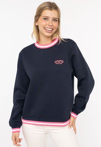 Marineblaues Sweatshirt mit einem kragen und Saum aus pink-weißen Streifen. Verziert mit kleinen roten Herzstickereien auf der Brust. Weicher Stoff, lässige Passform.