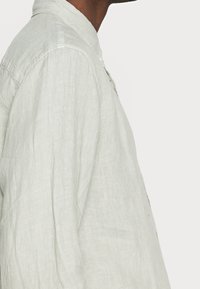 Jasnoszara lniana koszula z kołnierzykiem, z zapięciem na guziki i długimi rękawami, charakteryzująca się teksturowaną, lekko pomarszczoną powierzchnią.