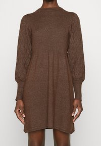 Robe marron tricotée avec un corsage côtelé et des manches bouffantes texturées à motif de losanges, s'arrêtant juste au-dessus des genoux.