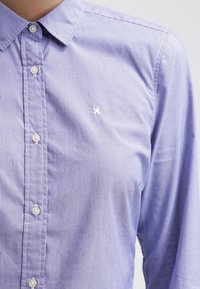 Camicia button-up a righe blu chiaro con colletto a punta, piccolo logo ricamato sul lato sinistro del petto e bottoni perlati.