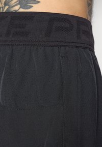 Svarta träningsshorts med ett strukturerat elastiskt midjeband, ventilerande perforerat tyg och slätt material med en sidoficka.