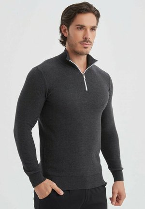 Sweat à fermeture éclair gris foncé avec un col haut, des poignets et un ourlet côtelés. Présente un accent zippé blanc au niveau du cou. Fabriqué à partir d'un tissu texturé.