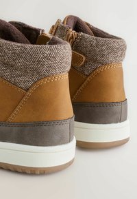 Bruna syntetiska läderankelboots med ett herringbone-tygkrage och gummisula. Har färgblockering i brunt och grått med vita accenter.