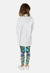 Hvid oversized skjorte med rygfald, farverige blomster-mønstrede leggings i blå og grøn, og hvide sneakers.