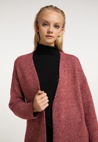 Cardigan într-o nuanță moale de roz heathered, cu un front deschis, mâneci lungi și o croială lejeră, combinat cu un guler înalt negru.