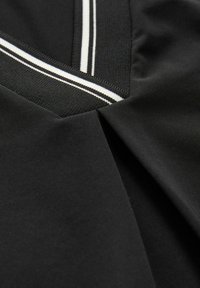 Tessuto nero con un pannello testurizzato caratterizzato da righe bianche. Il design include un collo a V e dettagli di pieghe sottili.