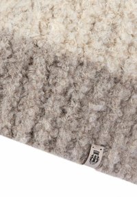 Textured wool rug featuring a gradient of cream to taupe colors, with a soft, plush feel and a small label in one corner.