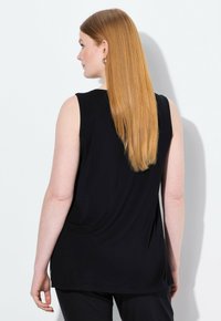 Top nero senza maniche con vestibilità morbida, caratterizzato da un collo rotondo e uno schienale drappeggiato. Tessuto morbido con una texture liscia e fessure laterali.