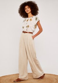 White short-sleeve shirt with palm tree print, beige wide-leg trousers with a brown belt, and brown woven sandals on a circular straw mat.