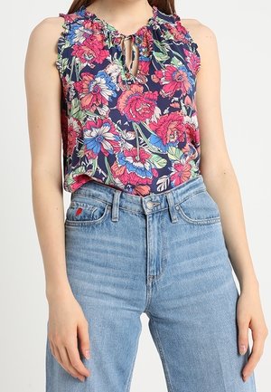 Blouse sans manches à fleurs roses, rouges et bleues, associée à un jean en denim bleu clair taille haute avec un petit détail en forme de cœur rouge.