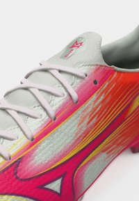 Κοντινό πλάνο γκρι ποδοσφαιρικού παπουτσιού με λευκά κορδόνια και ζωηρό πορτοκαλί, ροζ και κίτρινο γραφικό σχέδιο στο πλάι.
