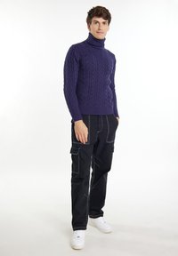 Maglione a collo alto, lavorato a maglia a trecce, di colore blu navy, con un design aderente. Abbinato a pantaloni cargo neri con cuciture bianche e tasche. Indossato con sneakers bianche.