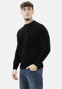 Maglione nero a collo rotondo in maglia con polsini e orlo a costine; indossato con jeans blu in denim. Presenta una finitura texture.