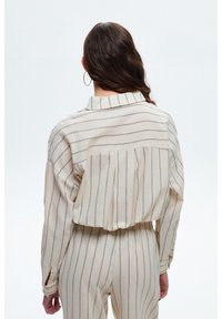 Blusa a righe beige chiaro con collo, maniche lunghe e vestibilità rilassata. Presenta strisce verticali blu navy e dettagli plissettati sul retro.