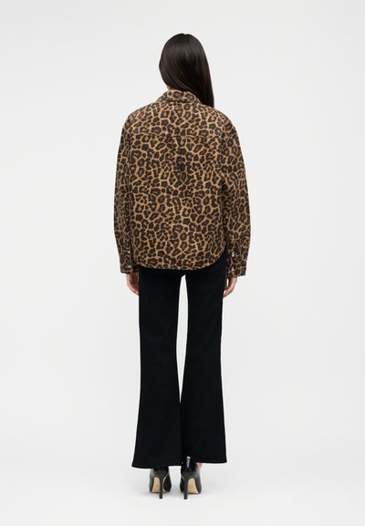 Woman facing away wearing a brown leopard print jacket, black flared pants, and black high heels on a white background.