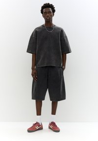 Felpa larga a maniche corte di colore grigio scuro con collo rotondo; abbinata a pantaloni corti grigio scuro. Indossata con scarpe sportive rosse e calzini bianchi.